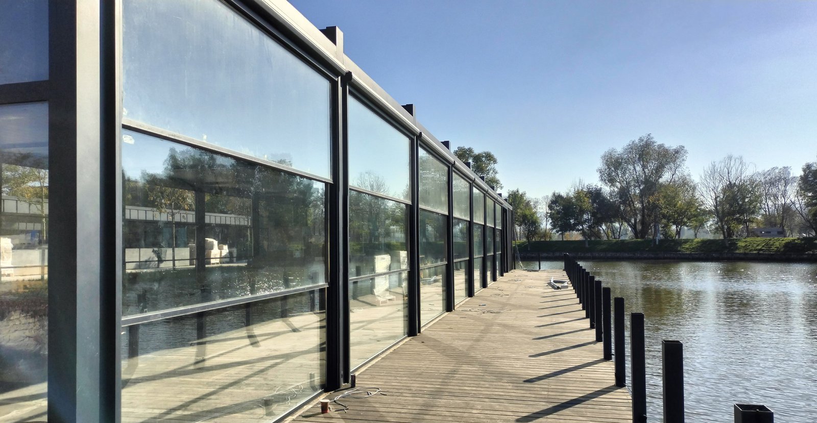 Glass walls of a waterfront restaurant along a wooden deck by a lake