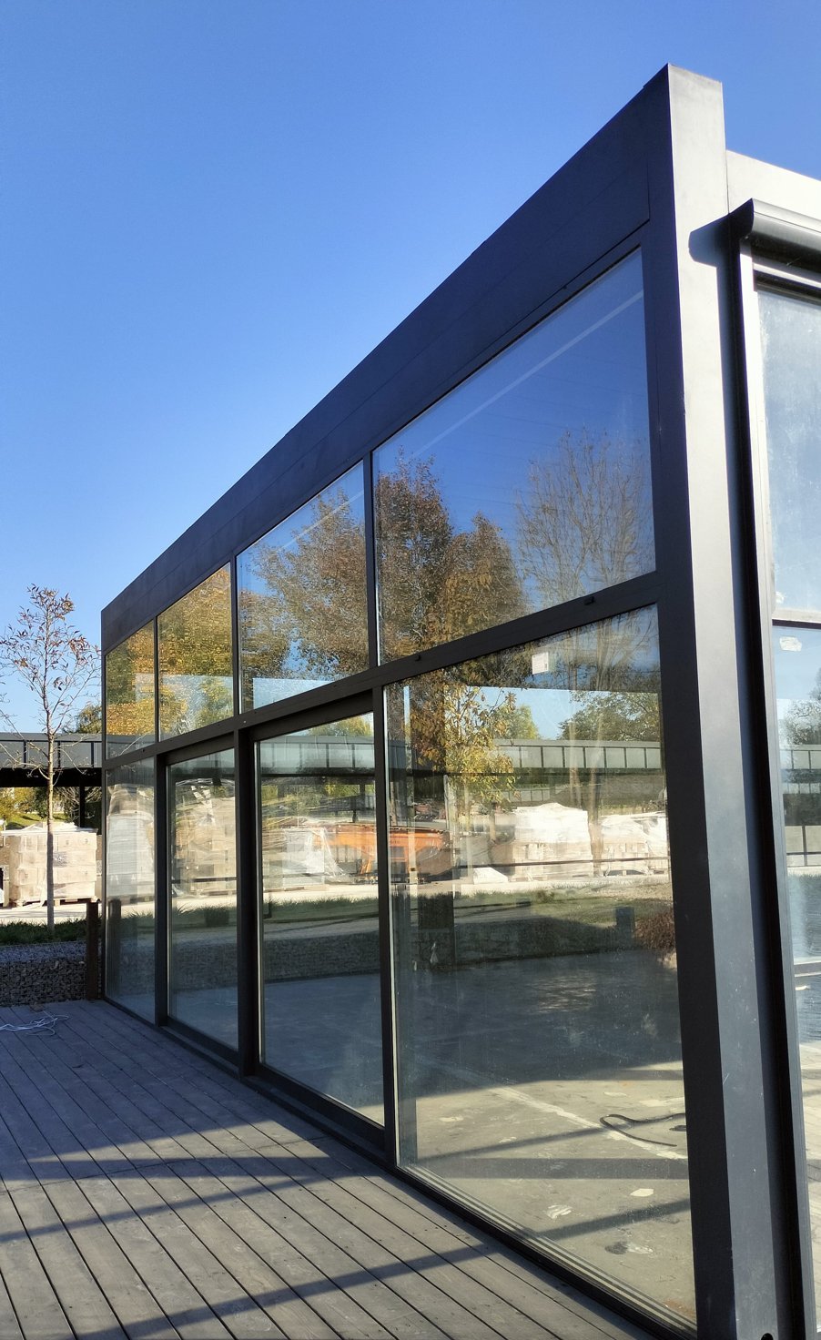 Floor-to-ceiling glass facade with dark aluminum frames on a lakeside deck