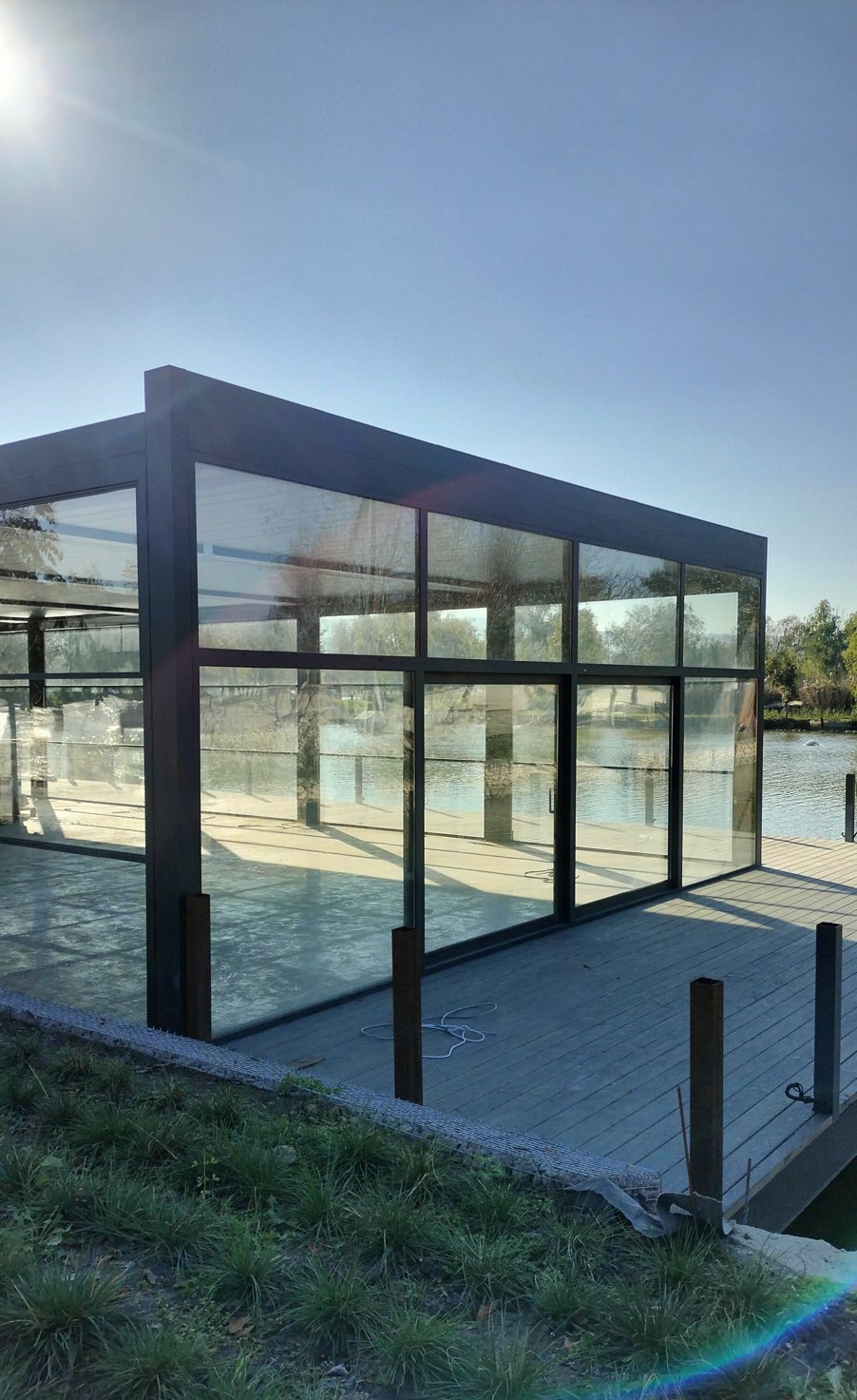 Glass pavilion with black aluminum frames next to a lake
