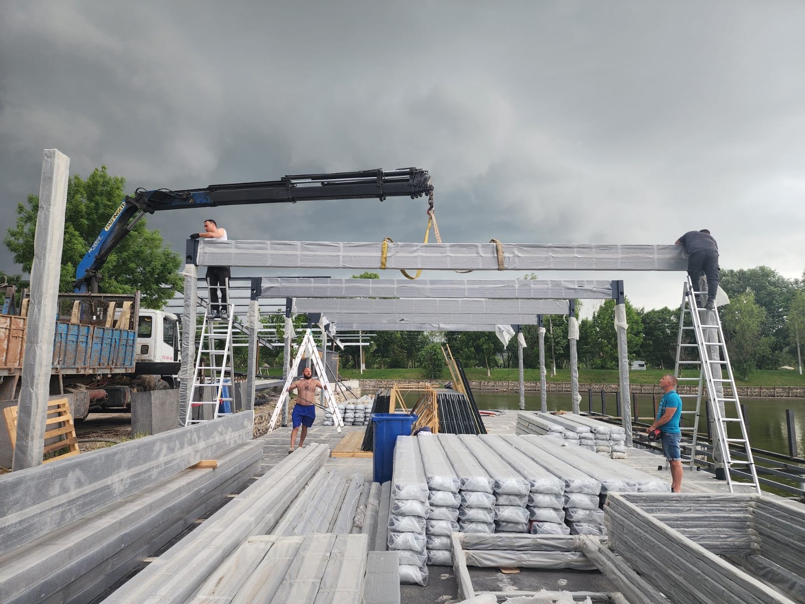 Crane lifting aluminum pergola beams into place on a lakeside deck