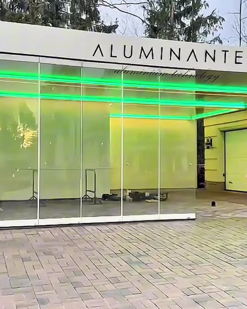 Garage enclosed with frameless folding glass under an ALUMINANTE pergola with green LED lighting