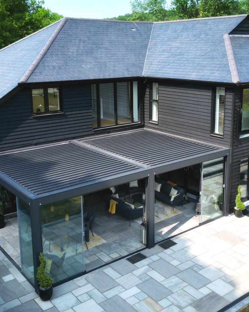 Louvered pergola with sliding glass walls across the back of a dark two-story house