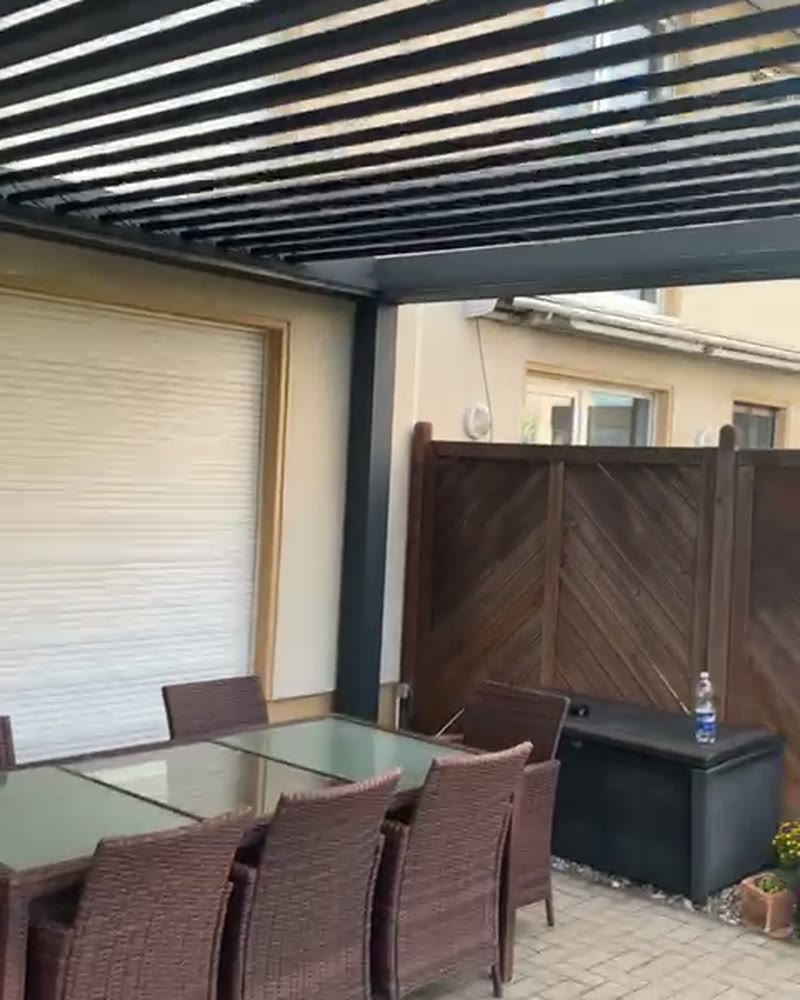 Louvered pergola over a dining table by a house wall