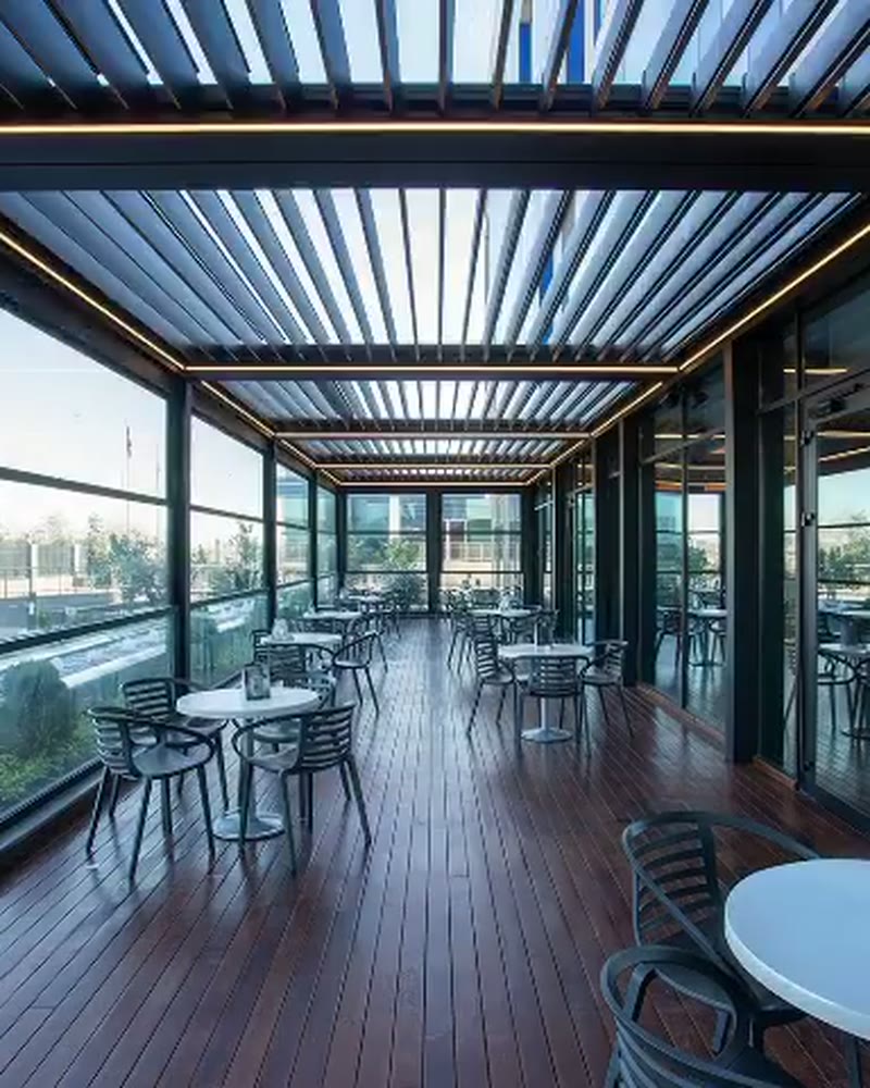 Restaurant under a louvered roof with floor-to-ceiling glass and city views