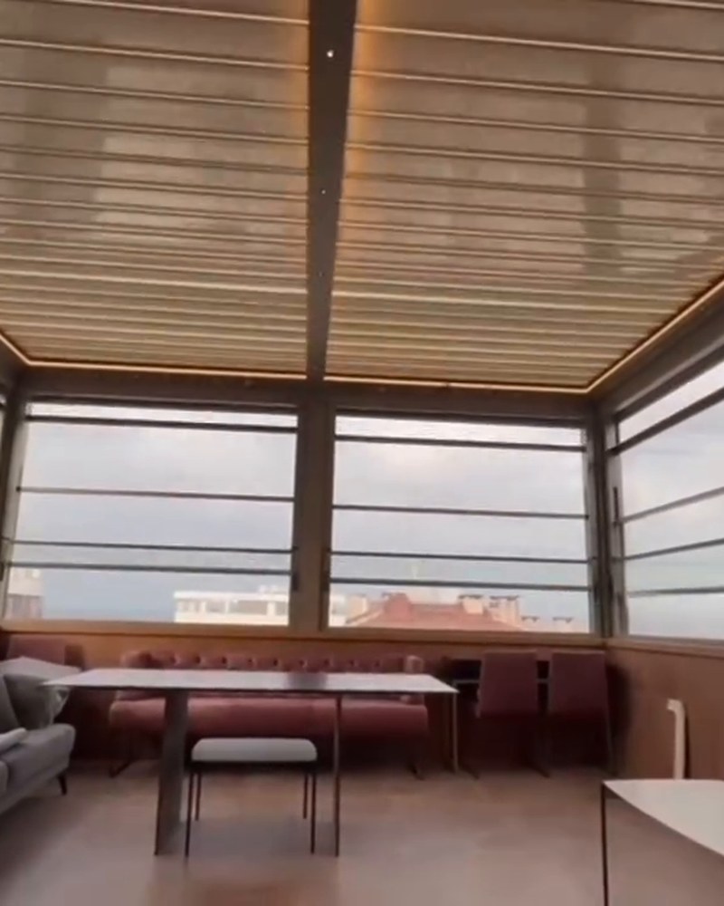 Rooftop lounge under a louvered roof with glass walls and sofas by the window