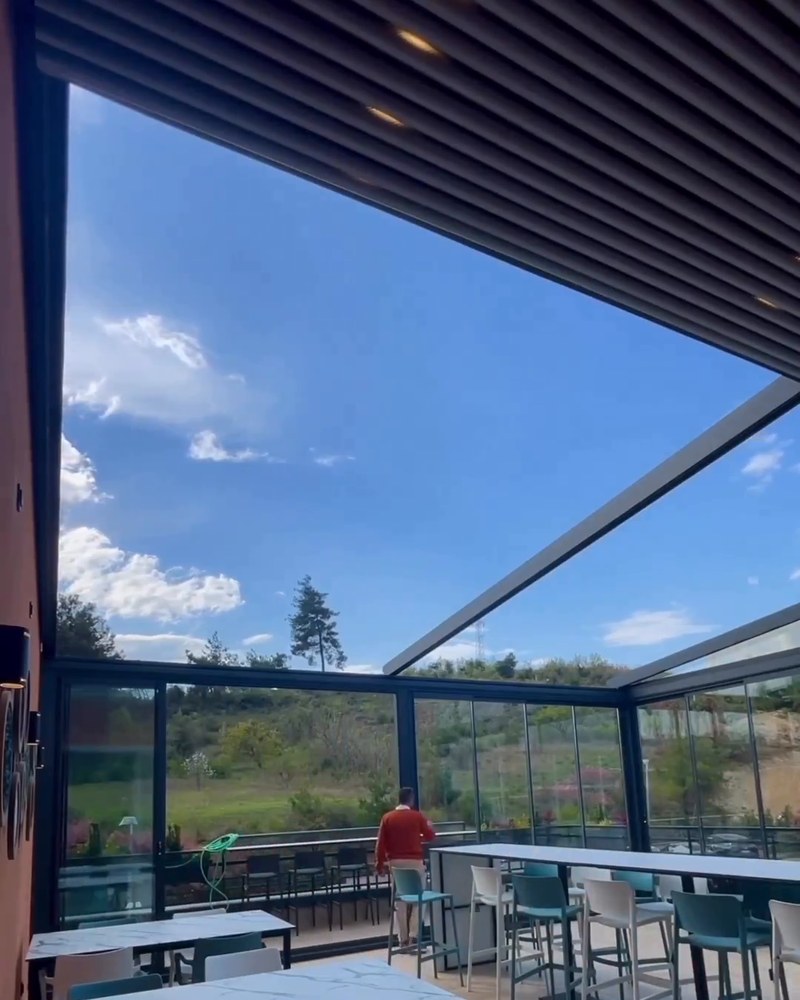 Restaurant terrace with the retractable roof opened to a blue sky and glass walls around the edge