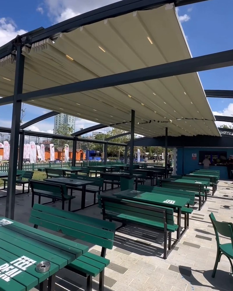 Long rows of green picnic tables under a double-pitched retractable fabric roof