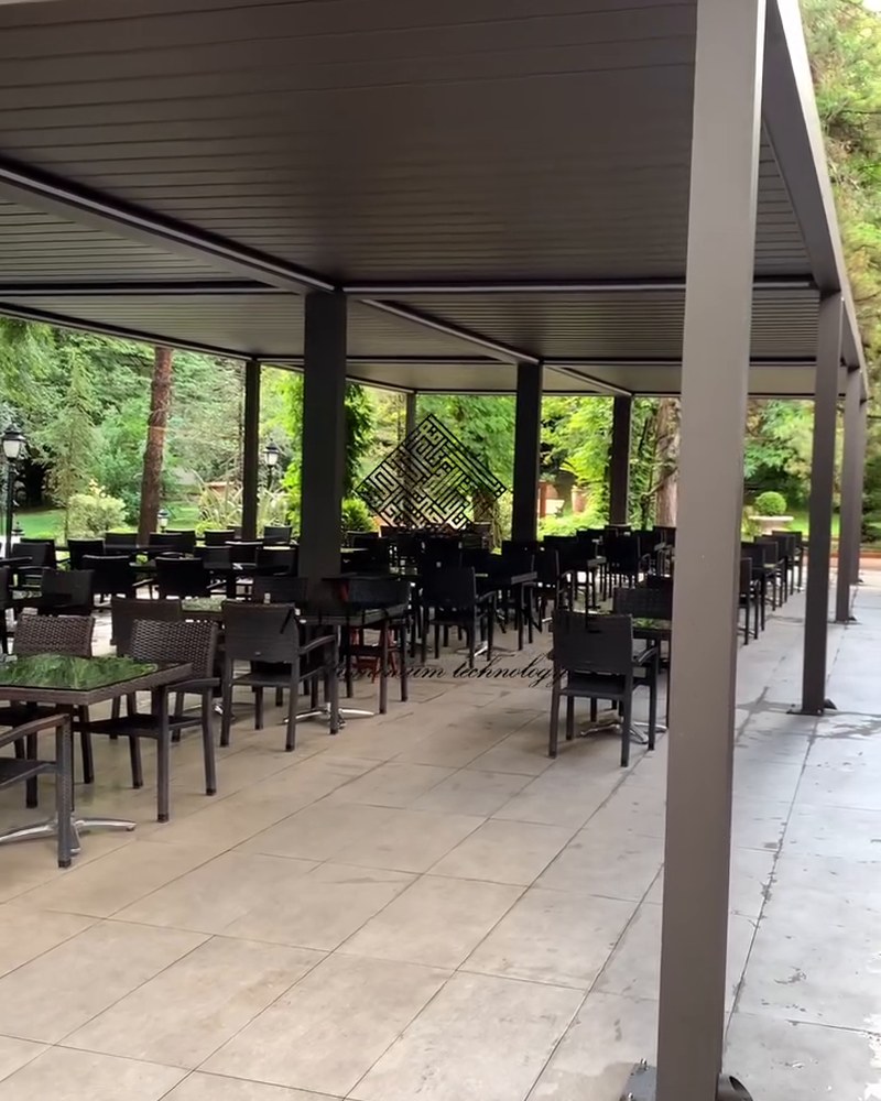 Rows of restaurant tables under long louvered pergolas among green trees