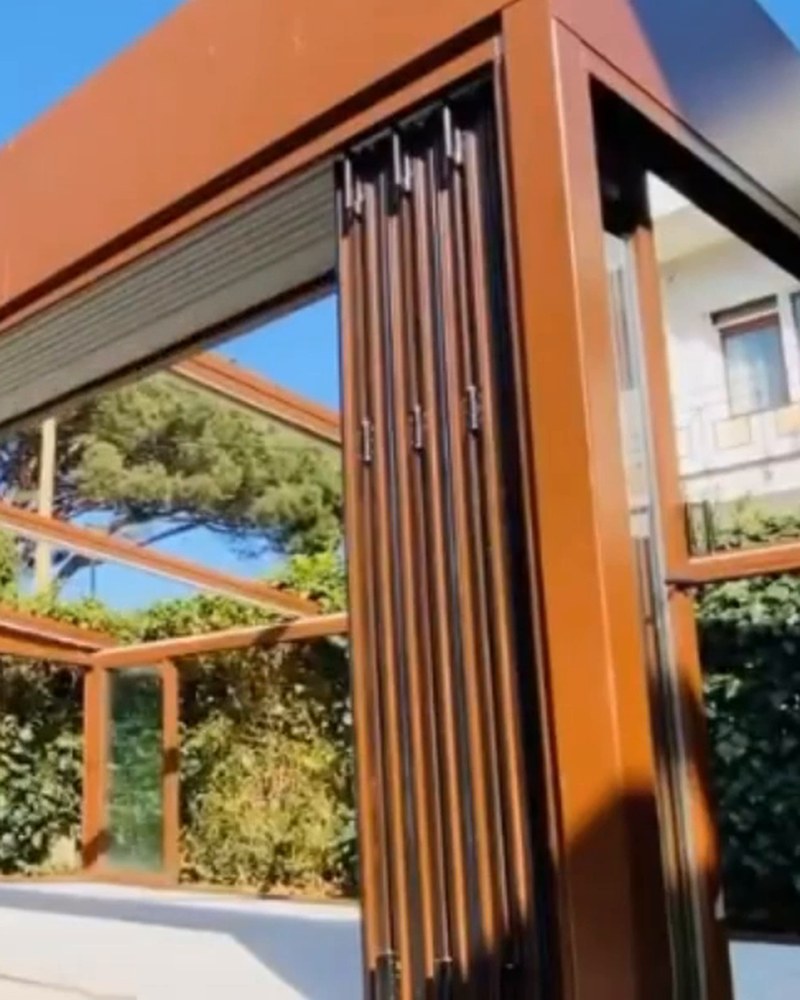 Bronze-colored pergola with folding glass doors stacked open at the corner