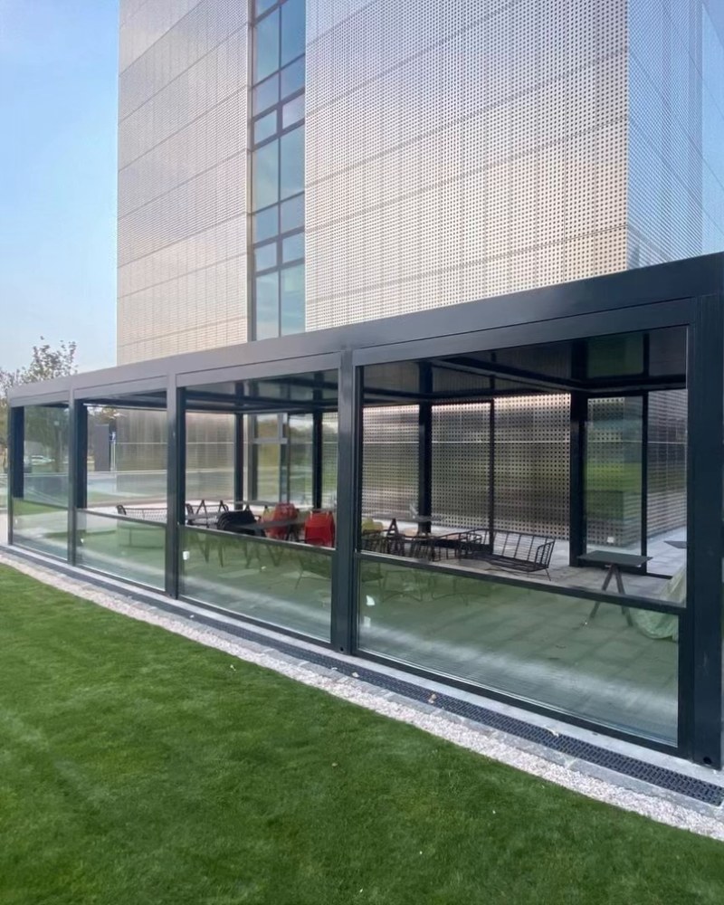 Glass-walled restaurant extension with black frames at the foot of an office tower