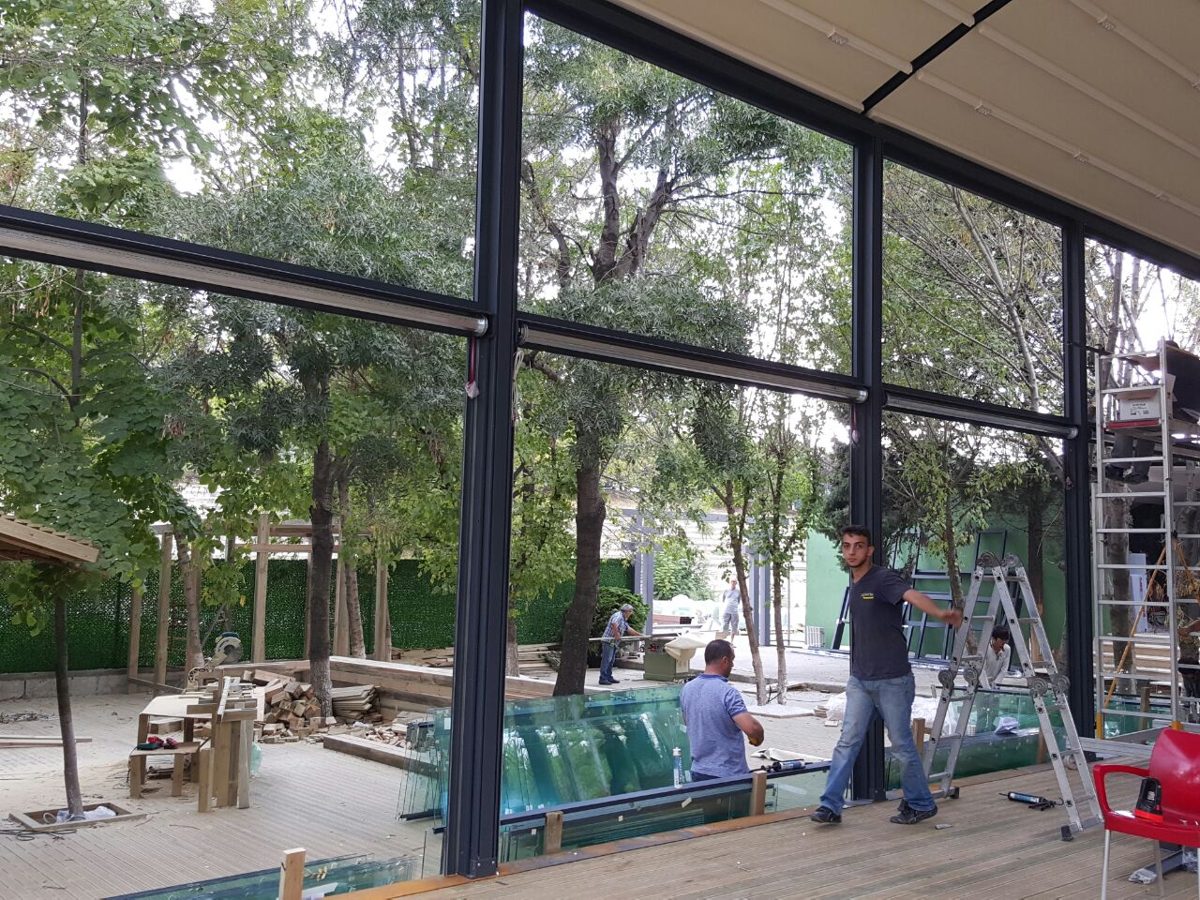 Glass panels being installed between aluminum posts on a restaurant terrace among trees