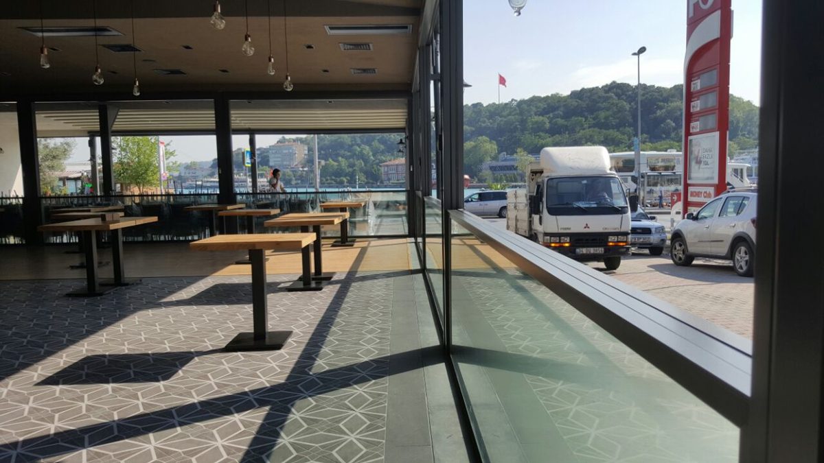 Glazed restaurant terrace with wooden tables and a view of the street
